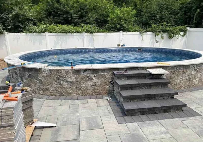 Stone-veneer pool wall with paver steps and a paver deck laid around it.
