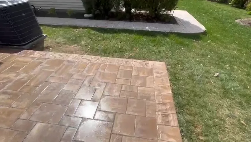 Large tan paver patio laid out beside a lawn and the back of the house.