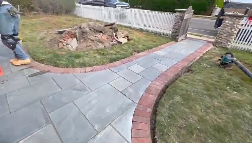 Bluestone front walk edged with a red brick course beside a white picket fence.