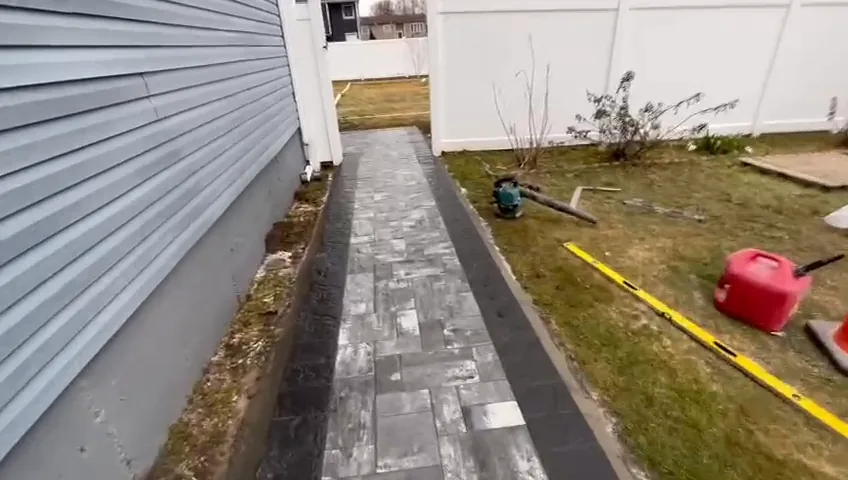 Narrow stone and paver walk along the side of a house, with the garden bed alongside.