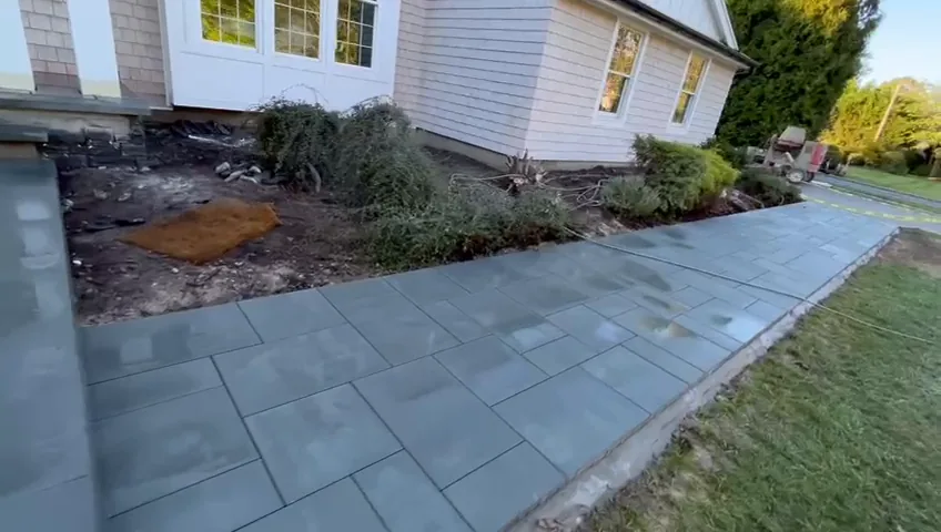 Bluestone patio slabs along the side of the house, with soil beds ready for planting.
