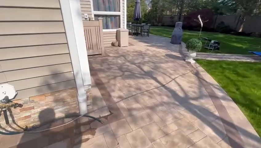 Covered paver patio beneath the house overhang, with a table and chairs beside the lawn.