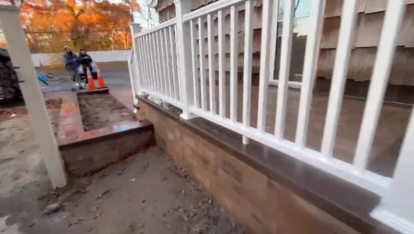 Block retaining wall with a white railing above and a brick terrace going in at its base.