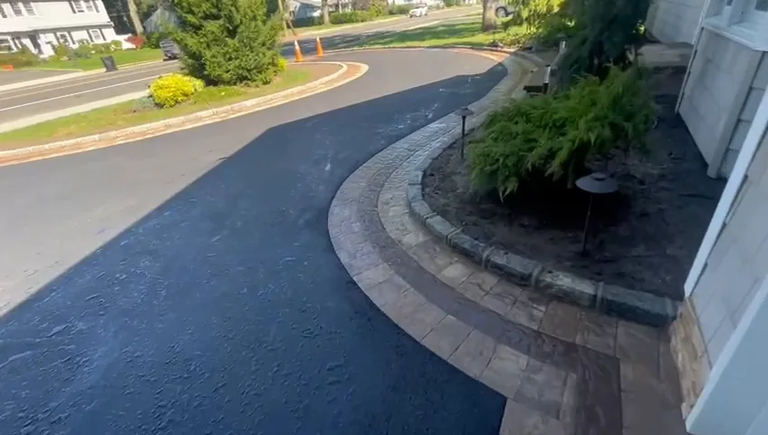 Fresh blacktop driveway meeting a paver apron at the edge of a property.