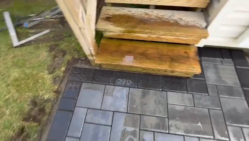 Paver patio under a deck, with a wooden stair coming down onto it.