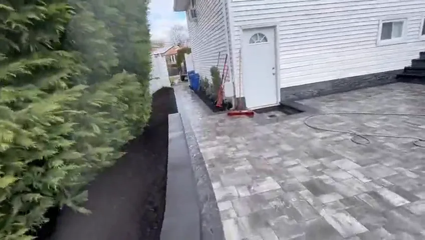 Paver path running along the side of the house, past a side door and a hedge, with the pool deck beyond.