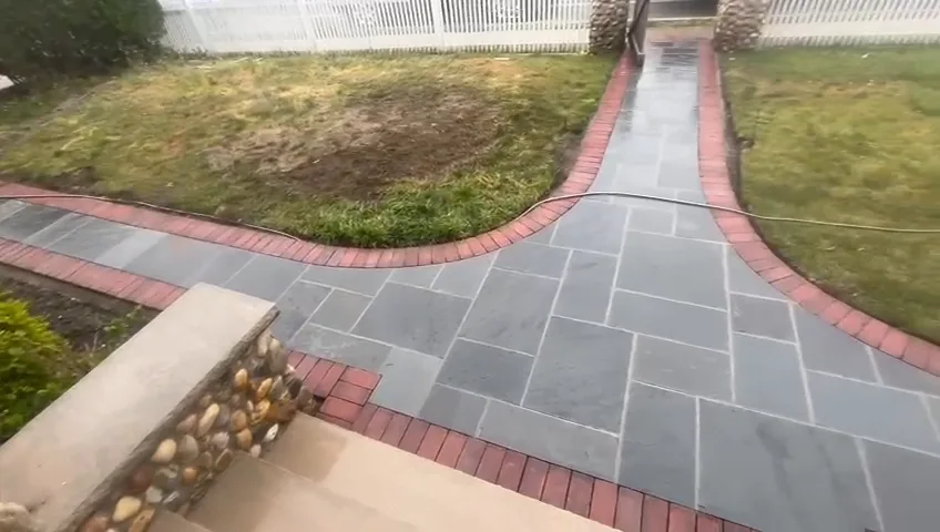 Paver walkway framed with a red brick soldier course, running between lawns and stone piers.